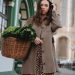 A woman in a brown coat carries a wicker basket of green vegetables while strolling through Erfurt, Germany.