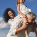 Grandparents playing with granddaughter outdoors under bright blue sky.