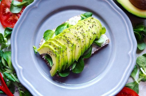 Delicious avocado toast with chia seeds and fresh tomatoes on a grey plate.