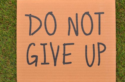 Cardboard sign reading 'Do Not Give Up' placed on green turf, symbolizing perseverance.